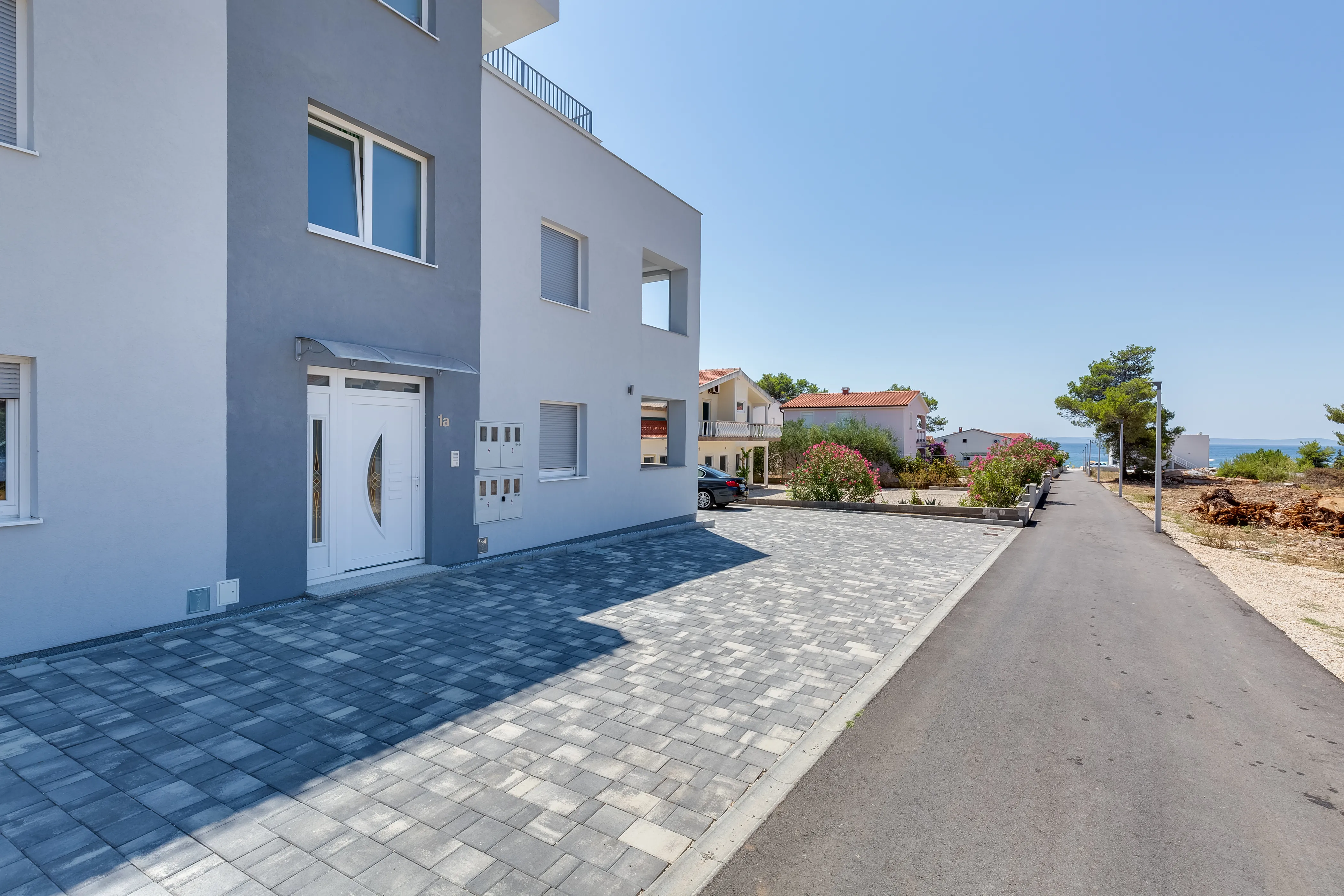 The apartment building and its paved driveway, with the sea at the end of the street